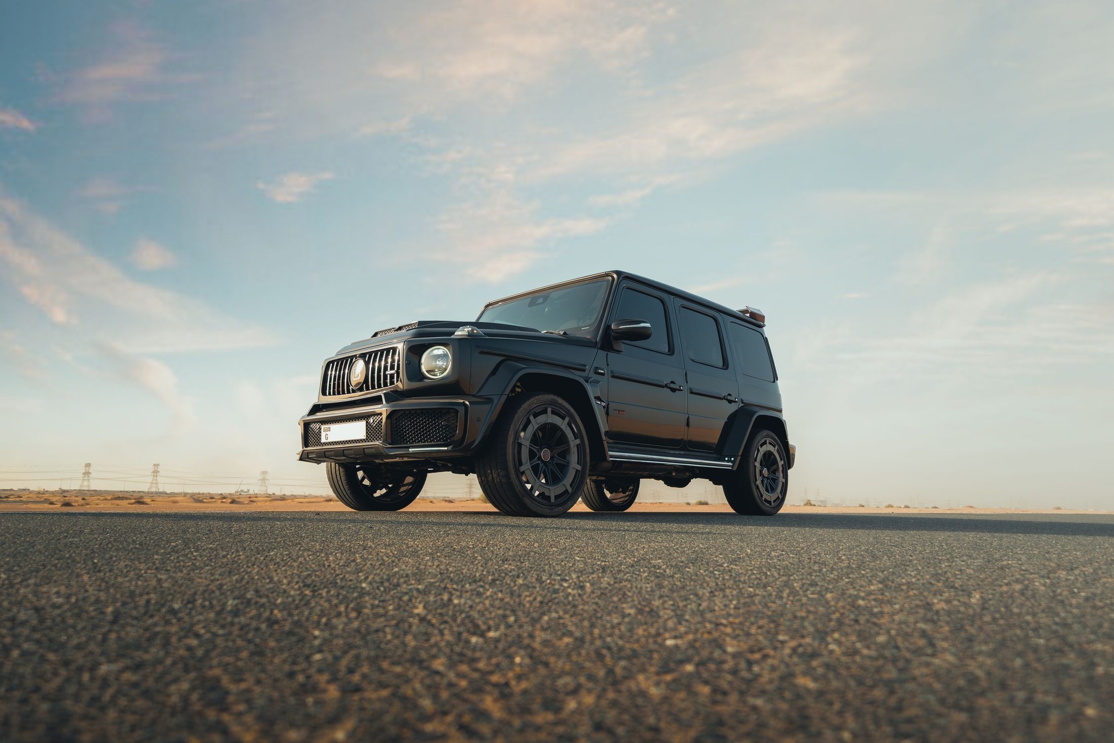 Black luxury SUV parked on a wide open road under a bright evening sky